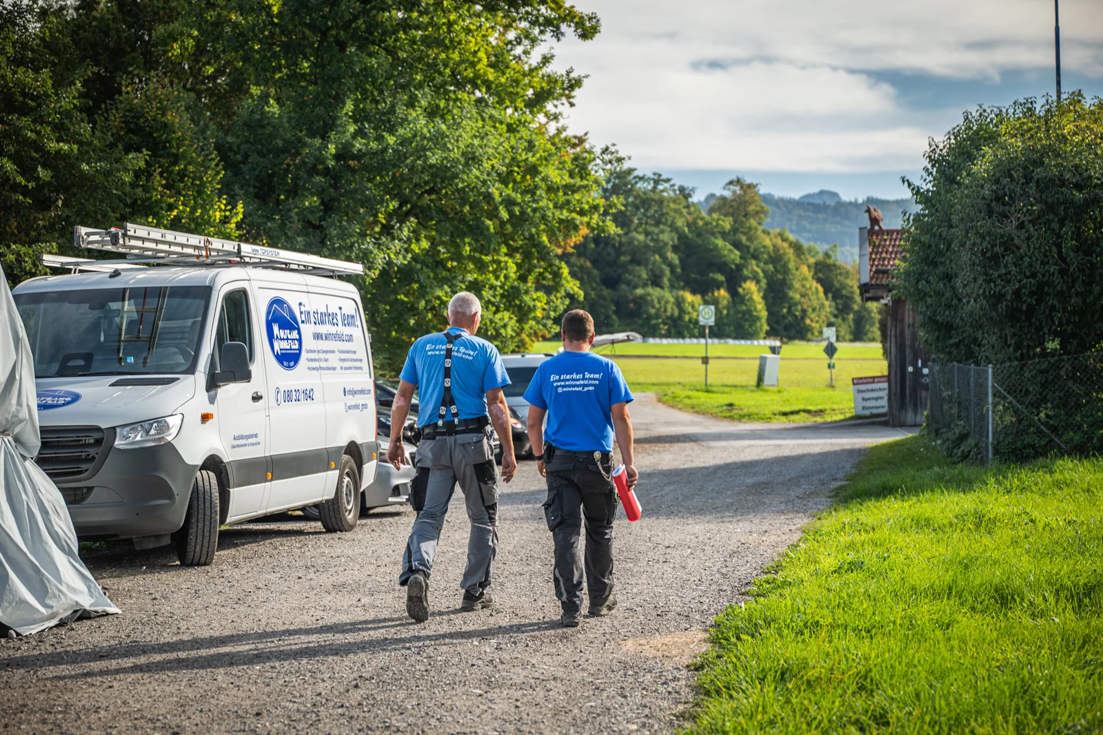 Zwei Kollegen von Winnefeld gehen im Abendlicht den Weg am Firmenwagen entlang